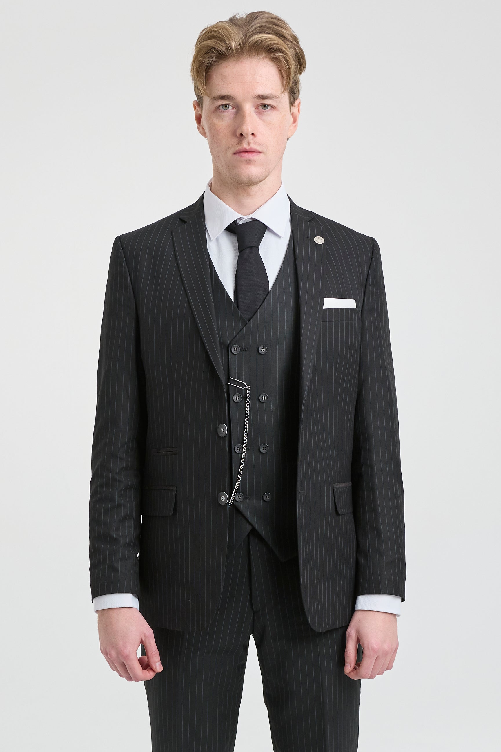 Man wearing a black pinstripe suit with a white shirt and black tie on a light gray background